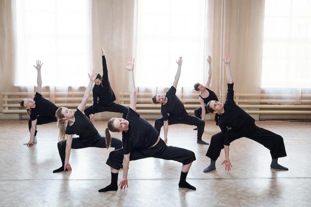 Grand groupe de jeunes en forme de vêtements de sport noirs exerçant ensemble pendant la formation sur le sol du studio de danse