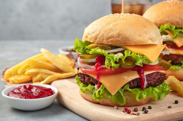 Grand hamburger avec galette de boeuf, fromage, sauce, légumes et salade sur fond gris. Vue latérale, gros plan.