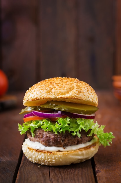 Grand hamburger de sandwich et hamburger avec du boeuf, des cornichons, de la tomate et du tartare sur fond de bois.