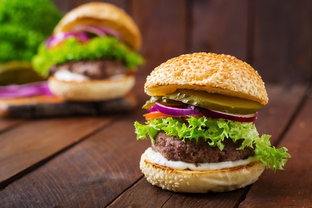 Grand hamburger de sandwich et hamburger avec du boeuf, des cornichons, de la tomate et du tartare sur fond de bois.