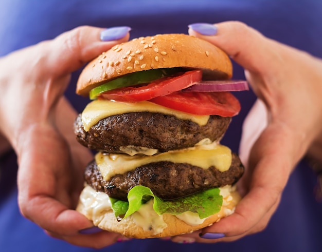 Grand hamburger de sandwich et hamburger avec sauce au bœuf, au fromage, à la tomate et au tartare dans les mains féminines