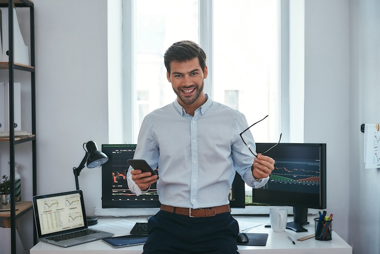 Photo grand heureux jeune homme d'affaires ou commerçant en tenues de soirée tenant des lunettes et un smartphone et souriant