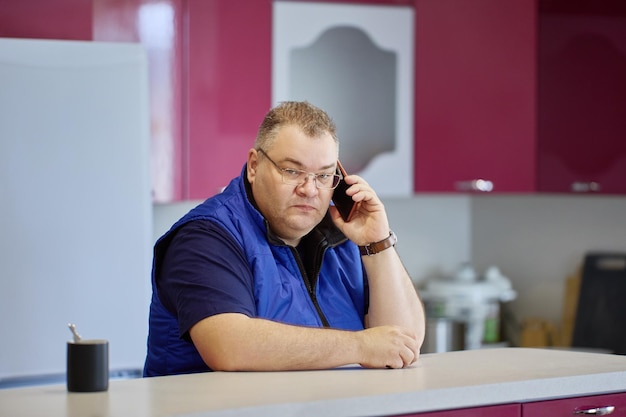 Photo un grand homme au visage tendu parle au téléphone dans la cuisine.