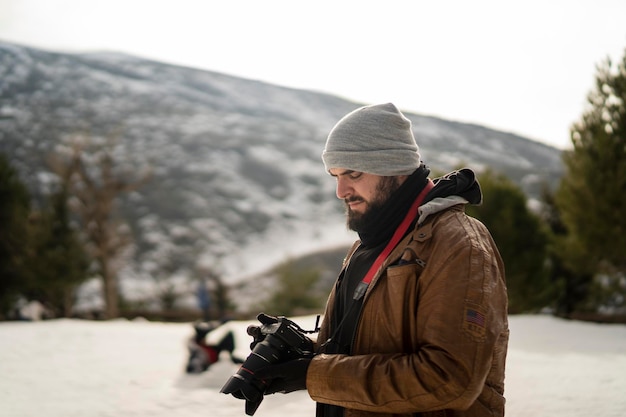 grand jeune homme avec barbe et appareil photo prenant des photos dans la neige