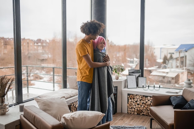 Grand jeune homme étreignant sa petite amie et la couvrant d'un plaid