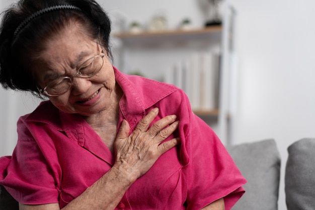 Une grand-mère âgée asiatique souffrant de douleurs cardiaques et tenant sa poitrine alors qu'elle est assise