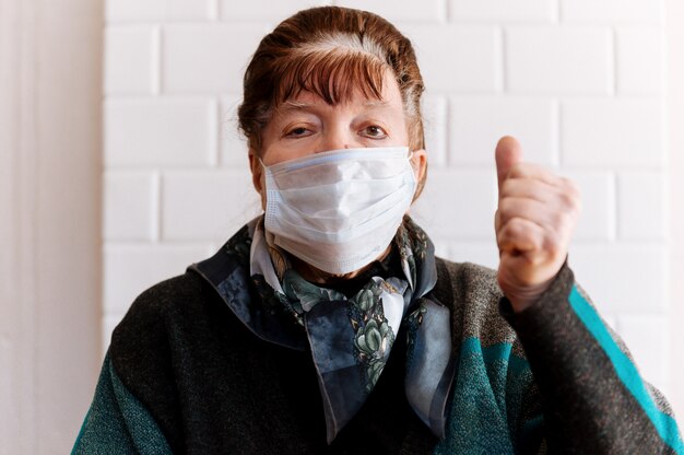 Grand-mère âgée avec un masque médical chirurgical montre un panneau d'arrêt sur l'appareil photo