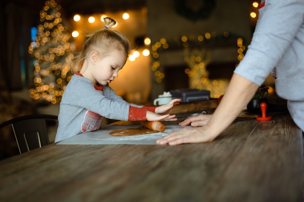 Une grand-mère aide sa petite-fille à dérouler la pâte pour un biscuit de Noël au gingembre traditionnel