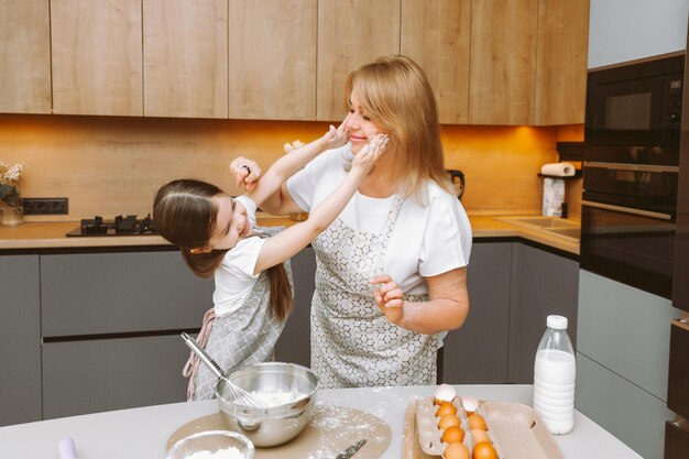 Une grand-mère attentionnée et une petite-fille s'amusent à faire des biscuits ensemble dans la cuisine de la maison Une grand-mère et une petite-fille âgées aimantes préparent un délicieux gâteau sucré