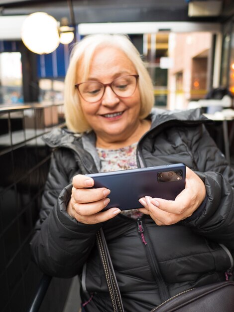 Photo une grand-mère blonde déconcentrée jouant sur son smartphone.