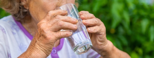 Grand-mère boit de l'eau dans un verre. Mise au point sélective. Femme.