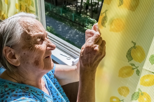 grand-mère coud un trou dans le rideau sur le balcon d'un immeuble