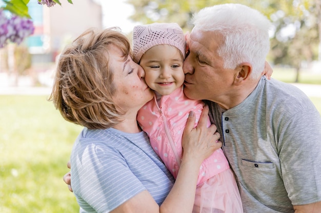 grand-mère et grand-père étreignent et tiennent une charmante petite-fille dans leurs bras promenade en famille