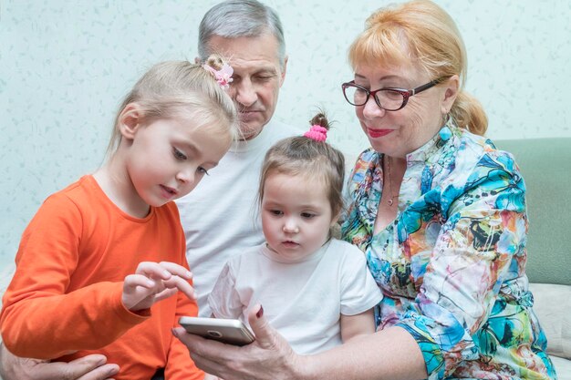 Grand-mère, grand-père et petites-filles avec un smartphone dans les mains sur le canapé