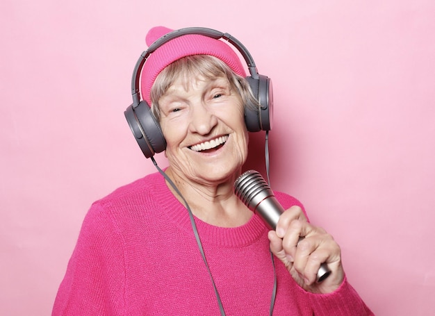 Grand-mère heureuse avec casque et microphone sur fond rose