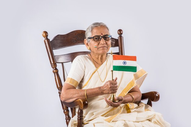 Grand-mère indienne célébrant la fête républicaine ou le jour de l'indépendance avec le visage peint avec des couleurs tricolores tout en tenant le drapeau national, isolé sur fond blanc