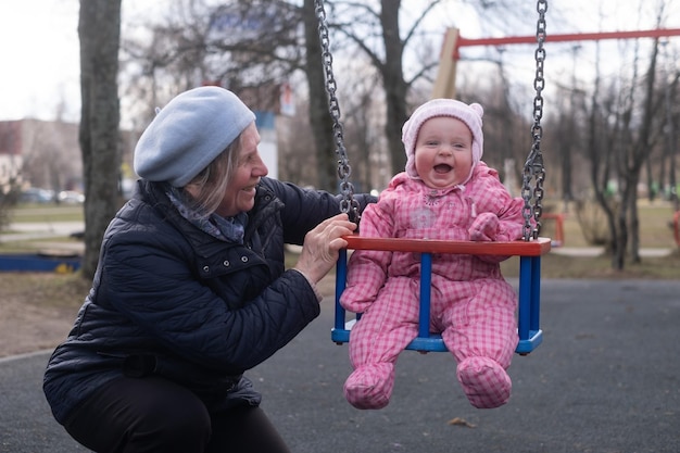 Grand-mère jouant avec sa petite-fille se balançant dehors dans le parc