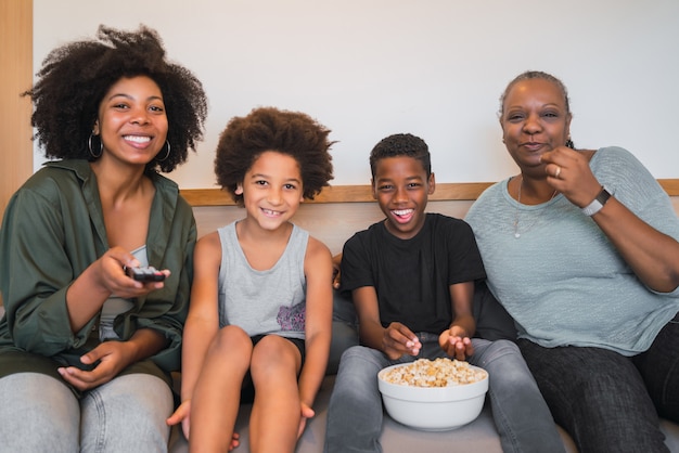 Grand-mère, mère et enfants regardant un film à la maison.