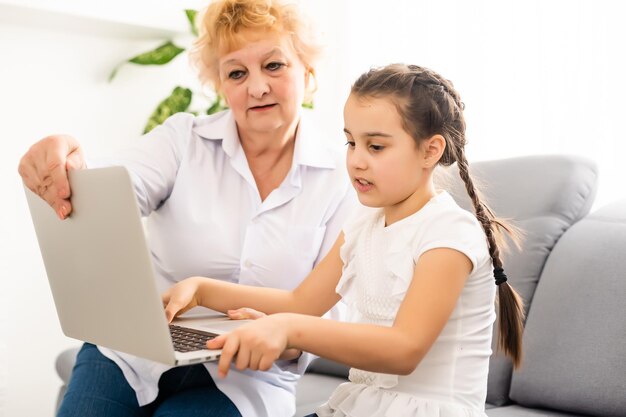 grand-mère moderne enseignant à son petit-enfant comment utiliser un ordinateur portable à la maison.