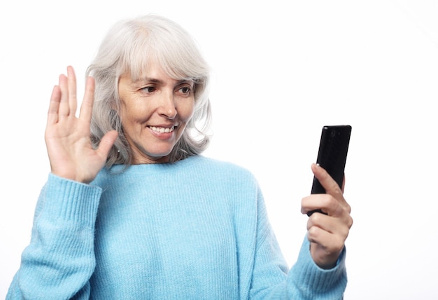 Grand-mère parle à ses petits-enfants par téléphone en souriant et en les saluant