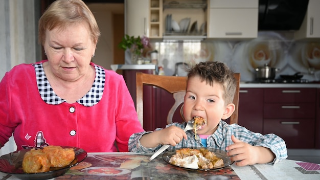 Grand-mère et petit-fils mangent à table.