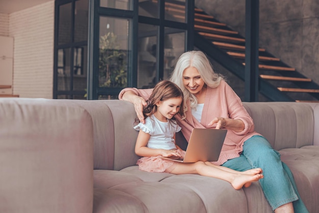 Grand-mère et petite-fille assises sur le canapé et utilisant un ordinateur portable à la maison