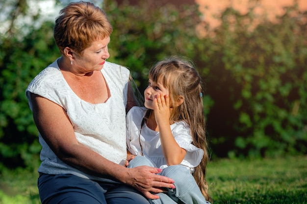 Grand-mère et petite-fille assises sur la pelouse un jour d'été La petite fille écoute attentivement sa grand-mère