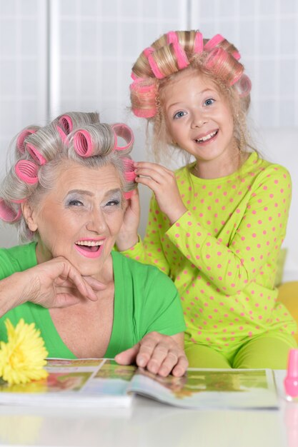 Photo grand-mère avec petite-fille à la maison faisant des cheveux bouclés