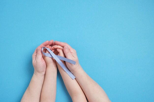 Grand-mère et petite-fille tiennent un ruban bleu sur fond bleu, les mains de l'enfant et les mains de la femme, l'espace de copie, le diabète et le symbole du cancer