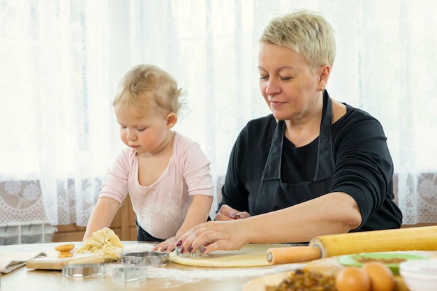 Grand-mère et petite-fille tranche une feuille de pâte avec un moule à biscuits