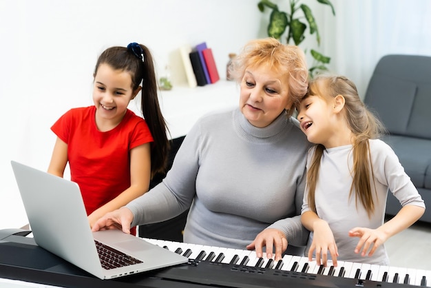 grand-mère et petites-filles apprennent à jouer du synthétiseur de piano sur un ordinateur portable en ligne à la maison.