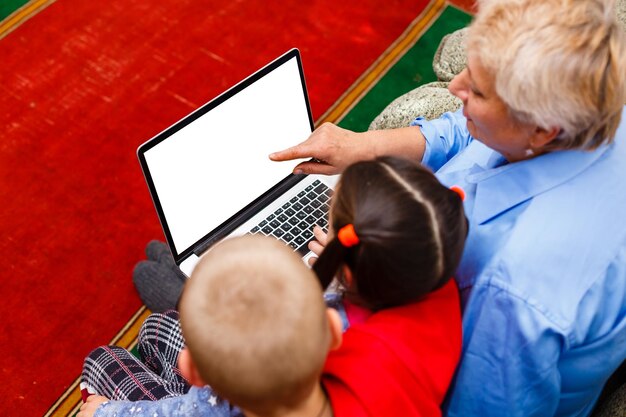 Grand-mère avec petits-enfants utilisant un ordinateur portable à la maison