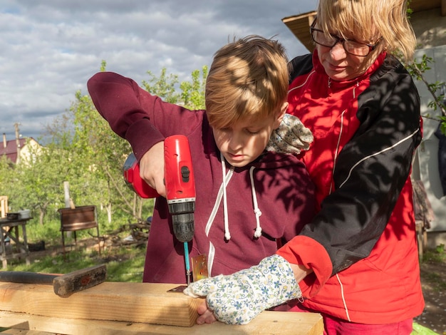 La grand-mère avec son petit-fils perçant du bois sur la table