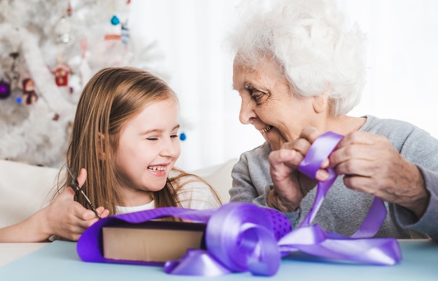 Grand-mère souriante avec petite-fille décorant des cadeaux ensemble à Noël