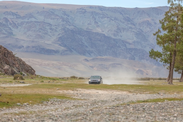 Un grand nuage de poussière de route derrière une voiture qui traverse la steppe. montagnes en arrière-plan