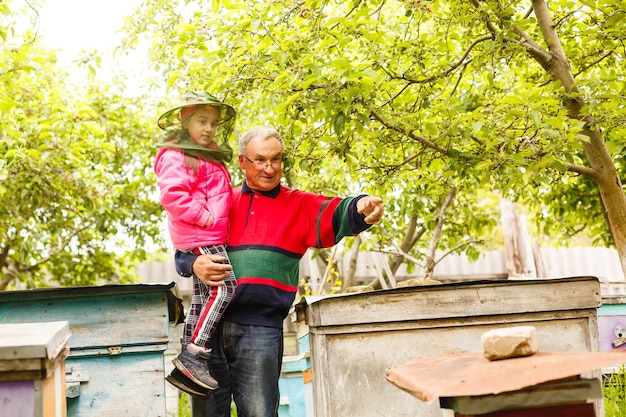 Un grand-père apiculteur expérimenté enseigne à sa petite-fille comment s'occuper des abeilles. Apiculture. Le concept de transfert d'expérience