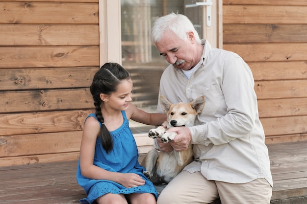 Grand-père assis avec sa petite-fille sur le porche avec chien à l'extérieur