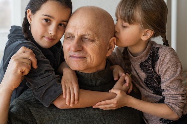 grand-père et deux petites-filles s'embrassant sur un canapé à la maison.