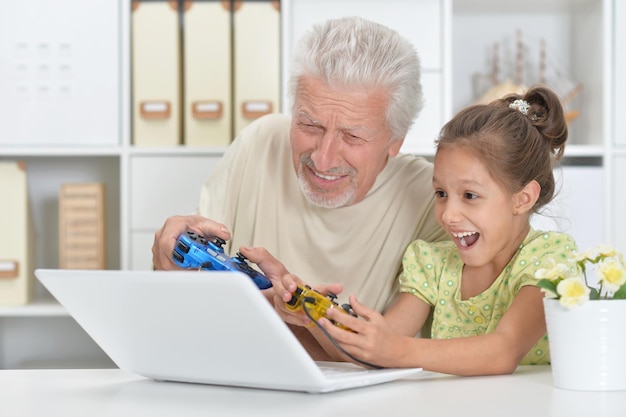 Grand-père émotionnel et petite-fille jouant à un jeu d'ordinateur avec un ordinateur portable