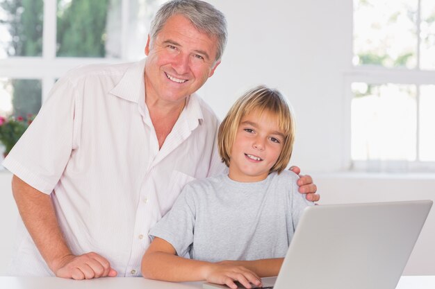 Grand-père et enfant regardant la caméra avec le sourire devant l&#39;ordinateur portable