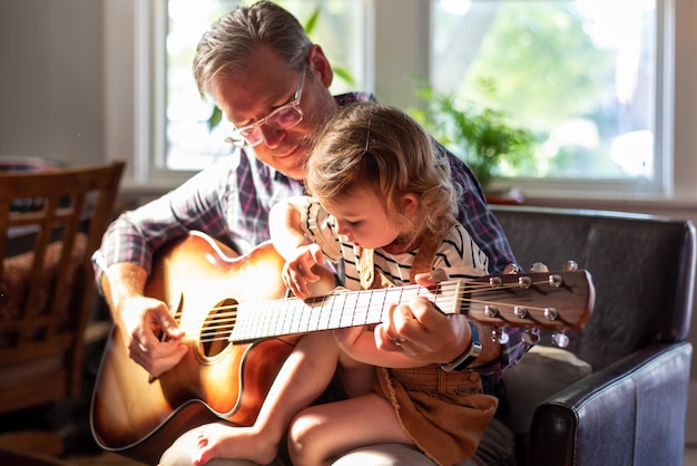 Un grand-père enseigne la guitare à sa petite-fille à la maison.
