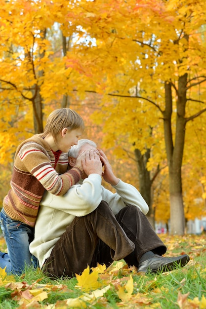 Grand-père avec un garçon se reposant dans un parc d'automne, le garçon ferme les yeux de son grand-père