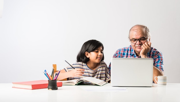 Grand-père indien enseignant sa petite-fille avec des livres, un crayon et un ordinateur portable, l'enseignement à domicile ou les frais de scolarité