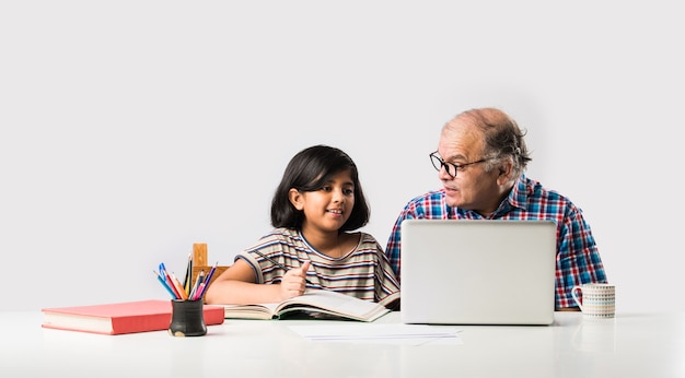 Grand-père indien enseignant sa petite-fille avec des livres, un crayon et un ordinateur portable, l'enseignement à domicile ou les frais de scolarité