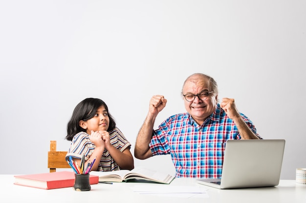 Grand-père indien enseignant sa petite-fille avec des livres, un crayon et un ordinateur portable, l'enseignement à domicile ou les frais de scolarité
