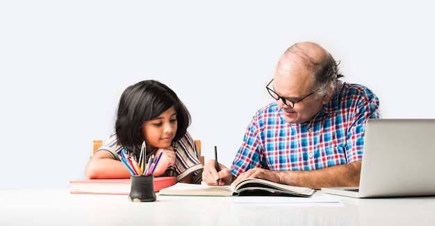 Grand-père indien enseignant sa petite-fille avec des livres, un crayon et un ordinateur portable, l'enseignement à domicile ou les frais de scolarité