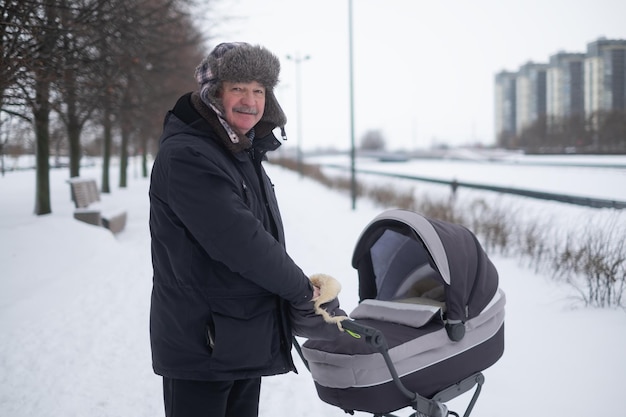 Grand-père marchant avec une poussette de bébé par une froide journée d'hiver enneigée