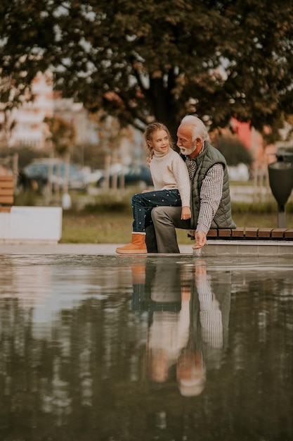 Grand-père passe du temps avec sa petite-fille au bord d'une petite piscine d'eau dans le parc le jour de l'automne