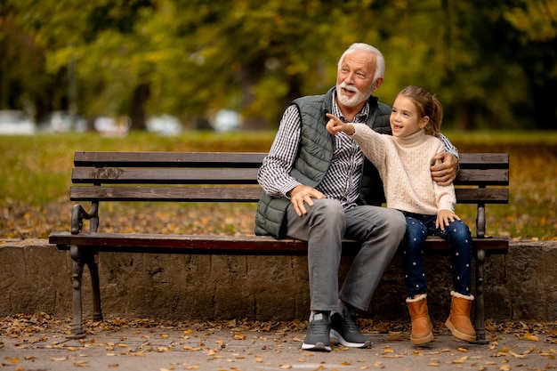 Grand-père passe du temps avec sa petite-fille sur un banc dans le parc le jour de l'automne
