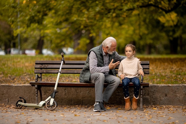 Grand-père passe du temps avec sa petite-fille sur un banc dans le parc le jour de l'automne